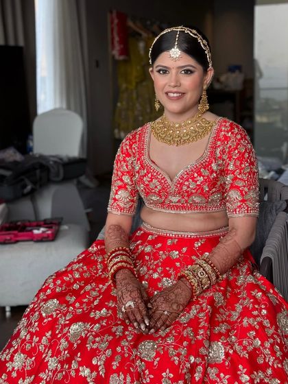 The bride, seated and smiling, looks the picture of happiness. Her traditional red and gold attire is perfectly complemented by her soft and radiant makeup.