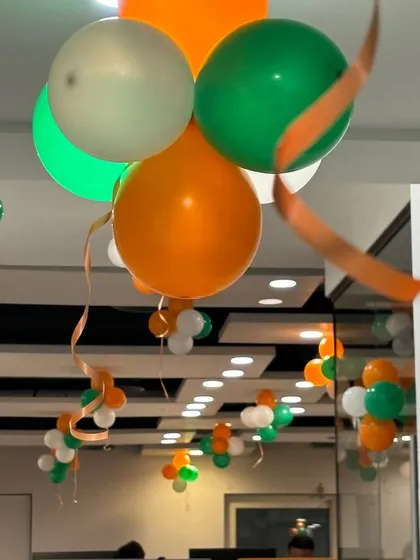A close-up of the helium balloon bunches used for the office ceiling decor. The combination of orange, white, and green balloons with flowing ribbons is a classic choice for national holidays.