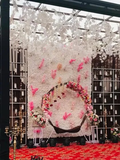 A wider view of the floral swing setup, showing the full backdrop and the overhead structure with hanging white leaves.