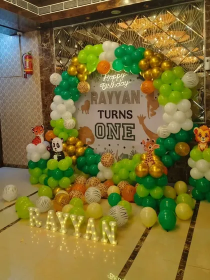 A jungle theme first birthday for Rayyan, featuring a balloon arch in green, white, and gold, animal cutouts, and his name in marquee lights.