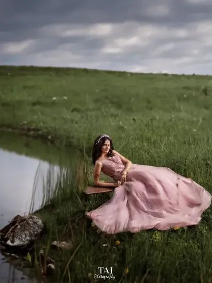 A creative and conceptual shot in a vast green field. The bride lies in her beautiful gown next to a mirror, creating a surreal and artistic portrait that blends nature with a touch of fantasy.
