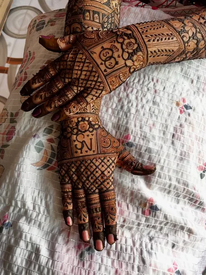 A detailed back-hand design for a bride, featuring the couple's initials 'S' and 'N' in a unique and artistic way. The surrounding patterns are a mix of floral and geometric elements.