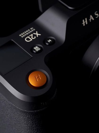 The orange shutter button is an iconic part of the Hasselblad design. This macro shot makes it the hero, using dark, moody lighting to draw attention to that single pop of color.
