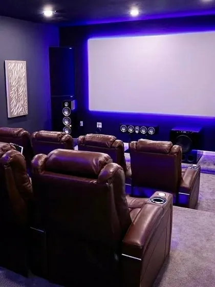 A showcase of a classic high-performance home theater setup. This room features plush leather recliners, a full array of freestanding tower and center channel speakers, and a dedicated subwoofer for impactful bass. The blue LED backlighting on the screen reduces eye strain and enhances perceived contrast.