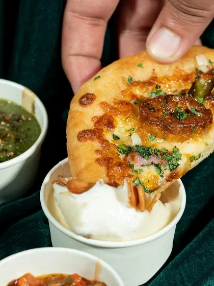 A close-up shot of khameeri bread being dipped into a creamy sauce. This action shot is designed to trigger a sensory response, making the viewer imagine the taste and texture.