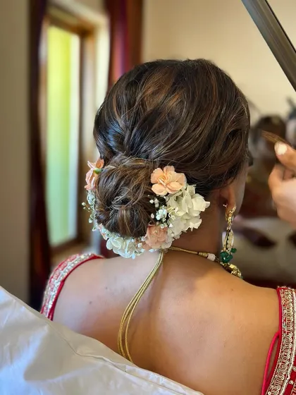 This intricate wedding bun is decorated with a mix of peach and white flowers, creating a soft and elegant look. It’s a perfect hairstyle for a bride wearing a traditional red lehenga.