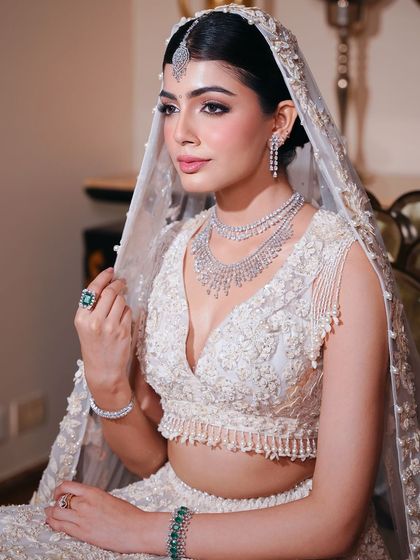 A magical, soft, and dewy bridal look perfect for a day wedding. The makeup gives a natural, glowing finish that enhances beauty without overpowering it, seen here on a bride in a stunning white lehenga.