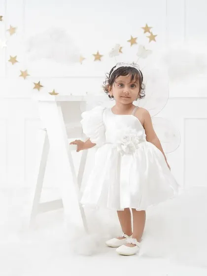 A full-length portrait of the little girl in her angel-like outfit, standing by a white ladder amidst dreamy clouds and golden stars.