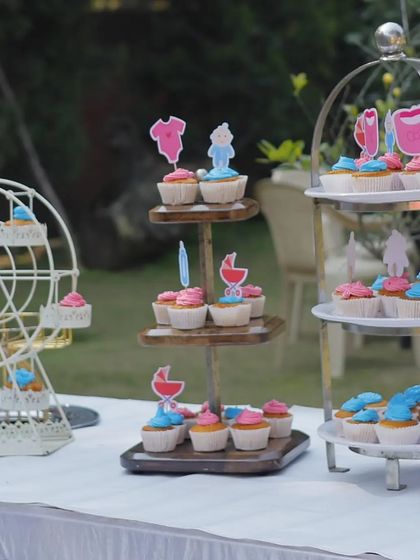 A whimsical dessert display for a baby shower. The setup includes a ferris wheel cupcake holder and tiered stands with pink and blue cupcakes to celebrate the upcoming arrival.
