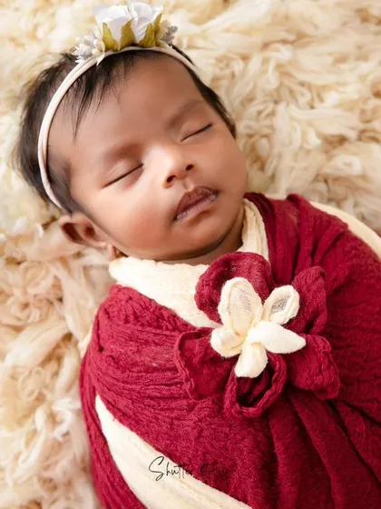 A slightly different angle of the red and cream floral wrap, highlighting the delicate headband and the baby's serene expression.