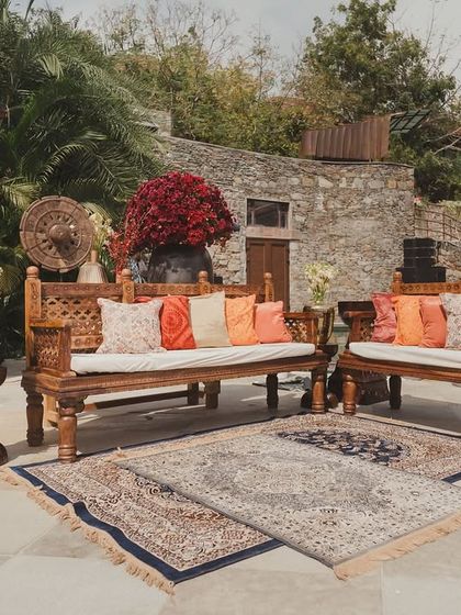 A rustic seating area at the 'Artisan's Studio' Mehendi, with carved wooden benches and layered carpets creating a cozy, bohemian vibe.