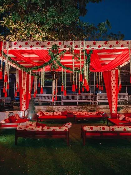 An intimate and traditional seating area for a pre-wedding ceremony. The design uses block-printed fabrics in red and white, with comfortable gaddas and hanging floral tassels.