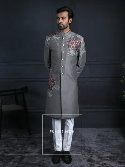 A full-length view of the charcoal grey achkan with vintage rose embroidery, paired with crisp white trousers for a modern, elegant look.
