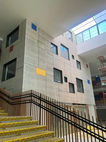 A new school building under construction, showing a feature wall with scattered, colorful window insets. This glimpse reveals how we integrate playful elements into the core architecture of the building.