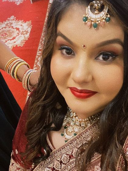 A happy client looking gorgeous in a red bridal outfit. She is wearing a heavy Kundan choker set with a matching crescent maang tikka.