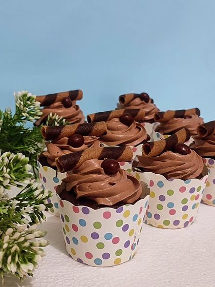 A batch of my classic chocolate cupcakes. Each one is topped with a swirl of rich chocolate frosting, a chocolate-covered coffee bean, and a decorative chocolate wafer roll.
