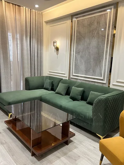 A deep green L-shaped sectional with quilted arm detailing, paired with a mustard yellow wingback chair. This combination of jewel tones and classic designs creates a rich and inviting atmosphere.