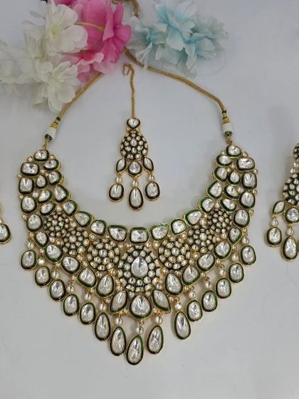 A heavy Polki necklace set with green enamel and cascading uncut stones, complete with matching earrings and maang tikka.