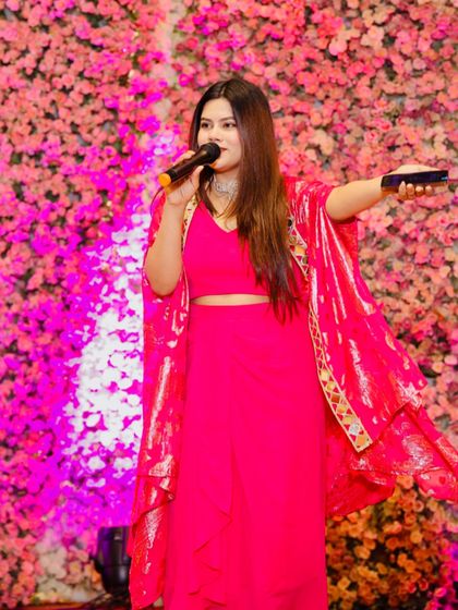 In action during a Sangeet night, wearing a vibrant pink outfit against a floral backdrop.