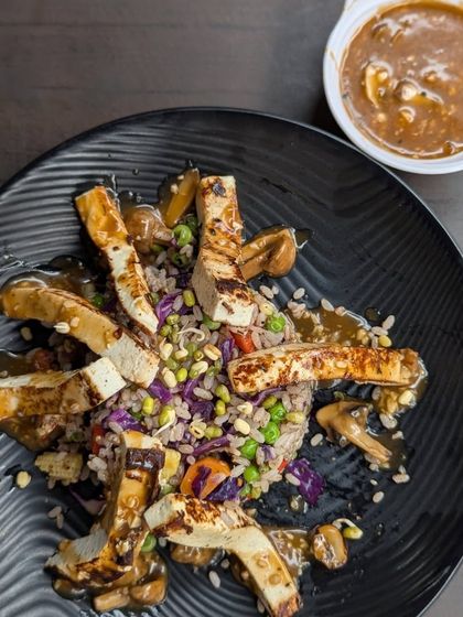 A plated meal of grilled chicken strips over a bed of seasoned rice and vegetables, with a side of sauce. This dish is a great example of a clean and satisfying post-workout meal.