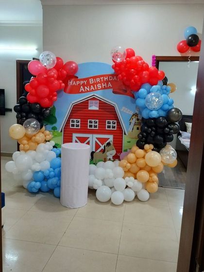 A charming farm-themed birthday party. This setup features a red barn backdrop surrounded by a colorful balloon arrangement, perfect for a fun and rustic celebration.