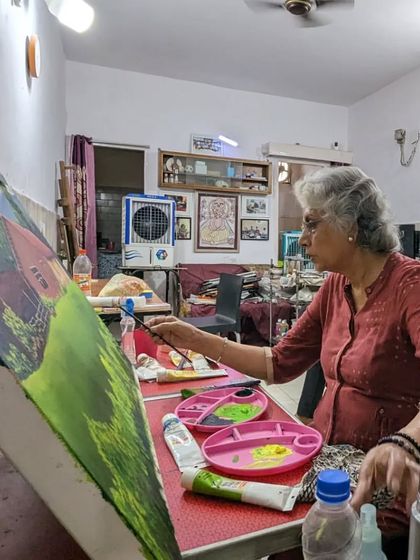 The artist at her easel. Harinder ma'am is fully engaged in painting her vibrant landscape, bringing the peaceful country scene to life.