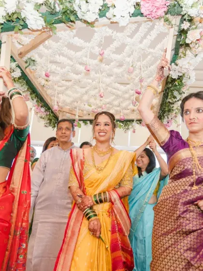 The bride's grand entrance at her Marathi wedding, walking under a floral canopy held by her family. Her radiant smile lights up the entire ceremony.
