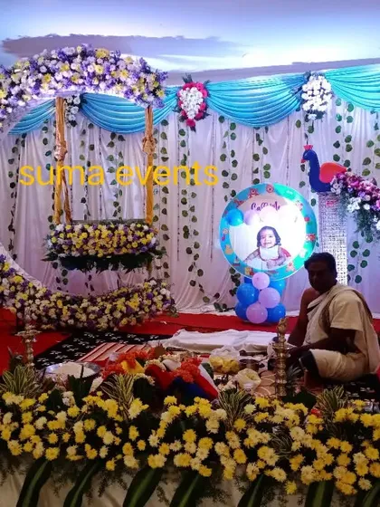 This is a popular naming ceremony stage design featuring a large crescent moon swing made of fresh flowers. The peacock motif and baby's photo add a personal touch to the celebration.