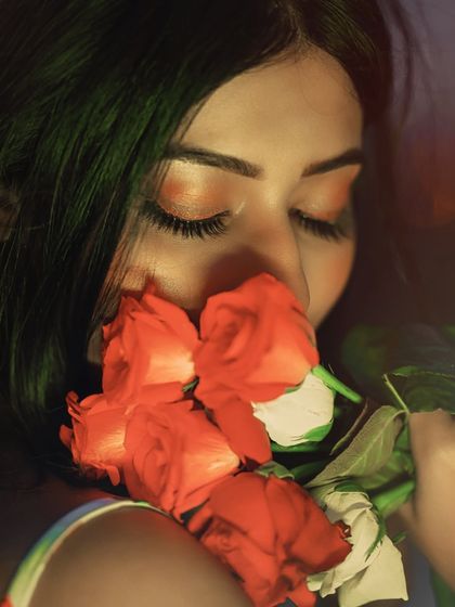 A stunning close-up beauty shot with a dreamy, ethereal glow. The way she smells the roses creates a sensory and romantic experience.