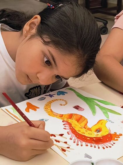 A student carefully adds details to her watercolor seahorse painting. This project helps them refine their brush control and understanding of color gradients.