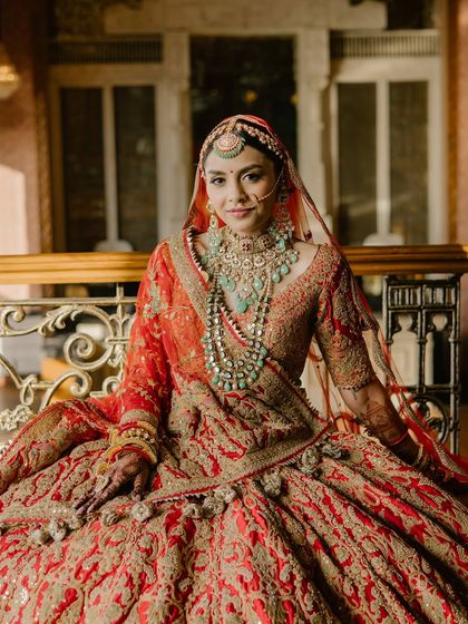 A full portrait of a bride looking like royalty. The makeup is balanced to complement the magnificent red and gold lehenga, ensuring the entire look is cohesive and breathtaking.