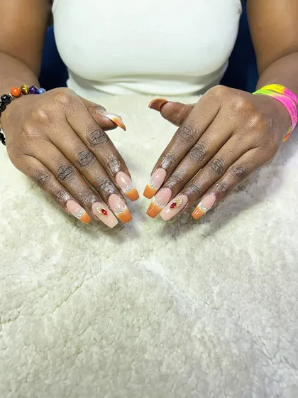 An orange glitter French tip with a single rhinestone accent. This is a warm and vibrant look, perfect for summer or festive occasions.