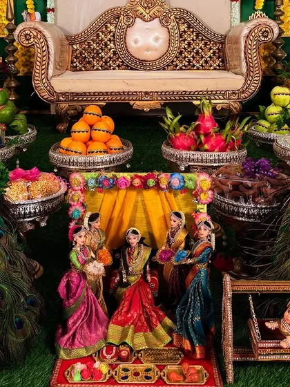 A closer look at the heart of the ceremony. This miniature doll scene depicts a traditional baby shower, surrounded by beautifully arranged fruits and sweets, guarded by elegant peacock figures.