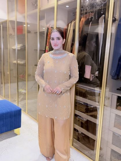 A full view of Shaista's sophisticated look in her walk-in closet. The neutral-toned outfit and minimal makeup are a perfect example of understated glamour.