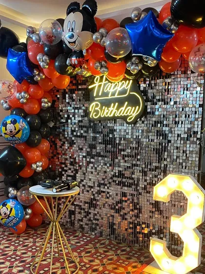 This view shows the full Mickey Mouse themed backdrop with the cake table and marquee number.