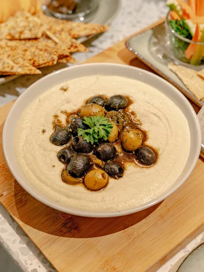 Our classic hummus, elevated with a topping of seasoned olives and a drizzle of high-quality olive oil. Served on a wooden board with crispy crackers, it's a timeless favorite for any occasion.