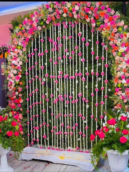 A simple and natural flower backdrop. This design features an arch of pink roses and greenery over hanging strings of jasmine and pink flowers.