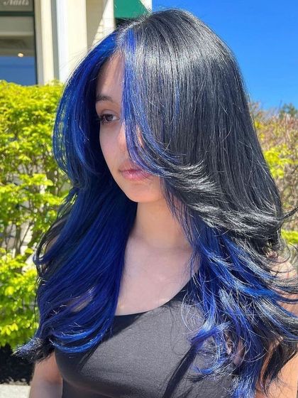 This face-framing blue hair color is a trend that's taking over. The bold blue against the client's natural dark shade makes her features pop and adds vibrancy to her layered haircut.