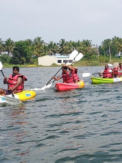 A line of tandem kayaks paddles across the water during a basic aqua sports course in Ambigarahalli, perfect for learning with a partner.