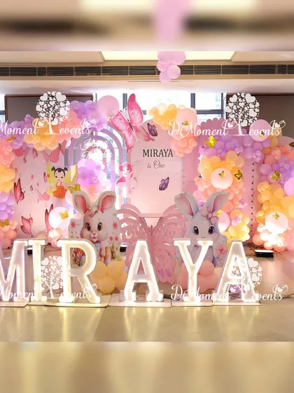 The main stage for Miraya's first birthday, featuring a whimsical theme with large bunny props, marquee letters, and a backdrop of pastel balloons and butterfly details.