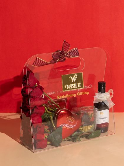 The "Love Affair" acrylic bag against a bold red background, highlighting its modern and chic design. It’s filled with Valentine’s essentials like roses, wine, and heart-shaped chocolates.