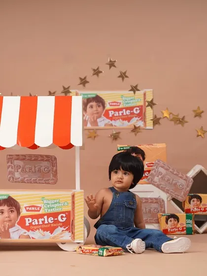 A wide shot capturing the entire Parle-G setup, with the baby girl looking off to the side, creating a candid feel.