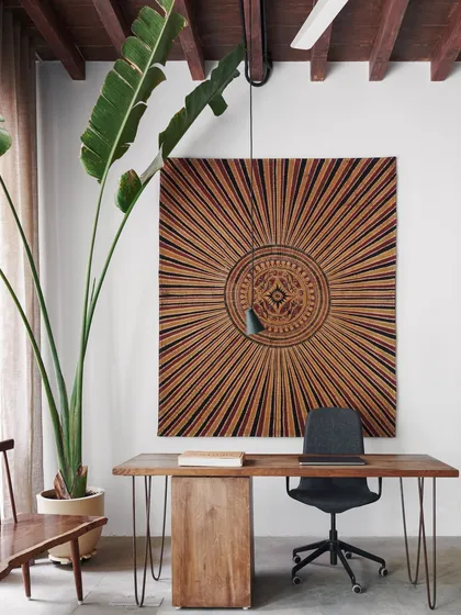 A corner of our studio, featuring a desk set against a large, intricate textile art piece. We believe in creating workspaces that are not just functional but also beautiful and inspiring.