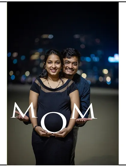 A beautiful night shot of a couple creating the word "MOM" with props, with city lights twinkling in the background.