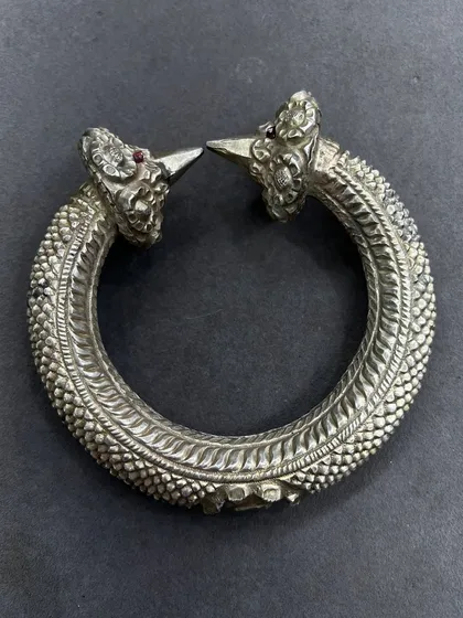 An exclusive silver leg kada, or anklet, with an antique finish. This piece features intricate scaling detail and two ornate heads with ruby-red stone eyes, a truly unique piece of tribal-inspired jewellery.