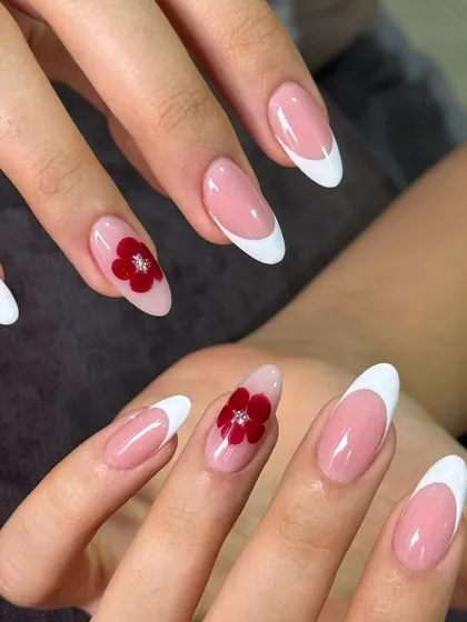 A timeless classic with a little twist. This is a clean, crisp white French manicure on elegant almond extensions, accented with a delicate, hand-painted red 3D flower.