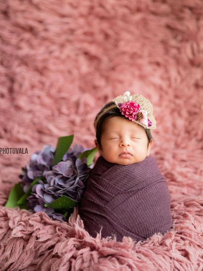 A sweet little newborn in a charming hat, nestled on a soft pink rug. The textures and colors come together to create a lovely portrait.