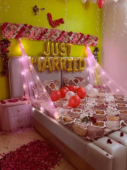 I also offer romantic room decoration for the wedding night. This setup features 'Just Married' foil balloons, a floral headboard arrangement, a canopy of fairy lights, and a path of rose petals for a truly special welcome for the newlyweds.