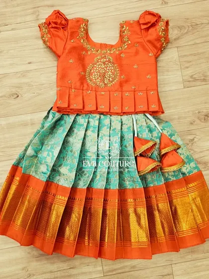 A flat-lay of a beautiful orange and sea-green Banarasi lehenga. The blouse features a pleated peplum and 'tree of life' embroidery.