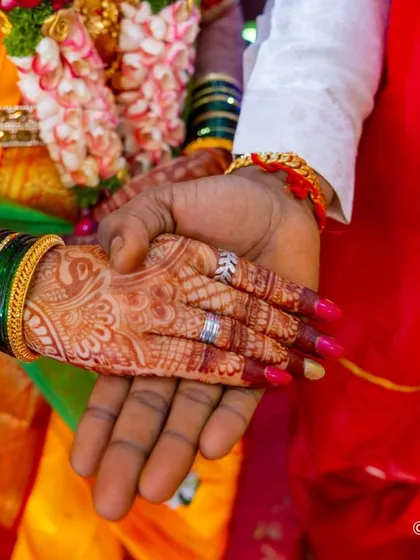 A close-up of a traditional Maharashtrian bride holding hands with her groom, showcasing her beautiful henna and vibrant pink nails that complete her wedding look.